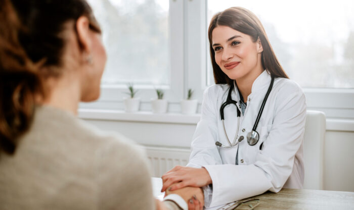 Friendly female doctor holding female patient's hand for encouragement and empathy.